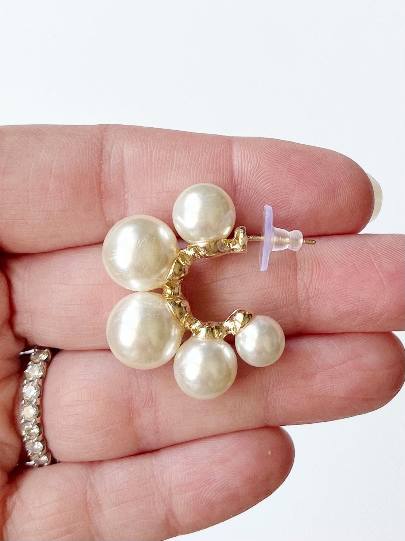 Pearl earrings held between fingers with a white background