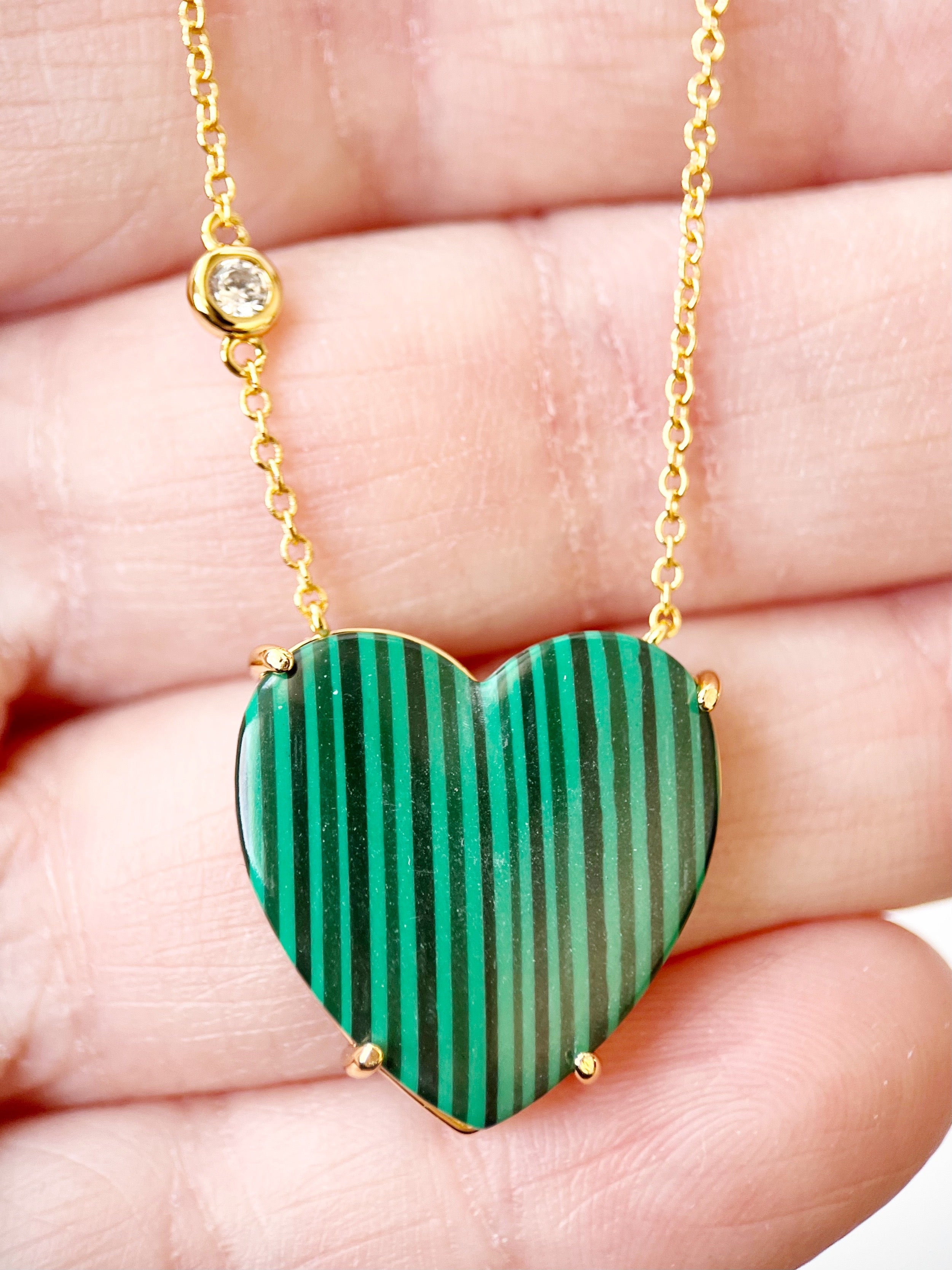 Heart-shaped malachite pendant on a gold chain held in hand