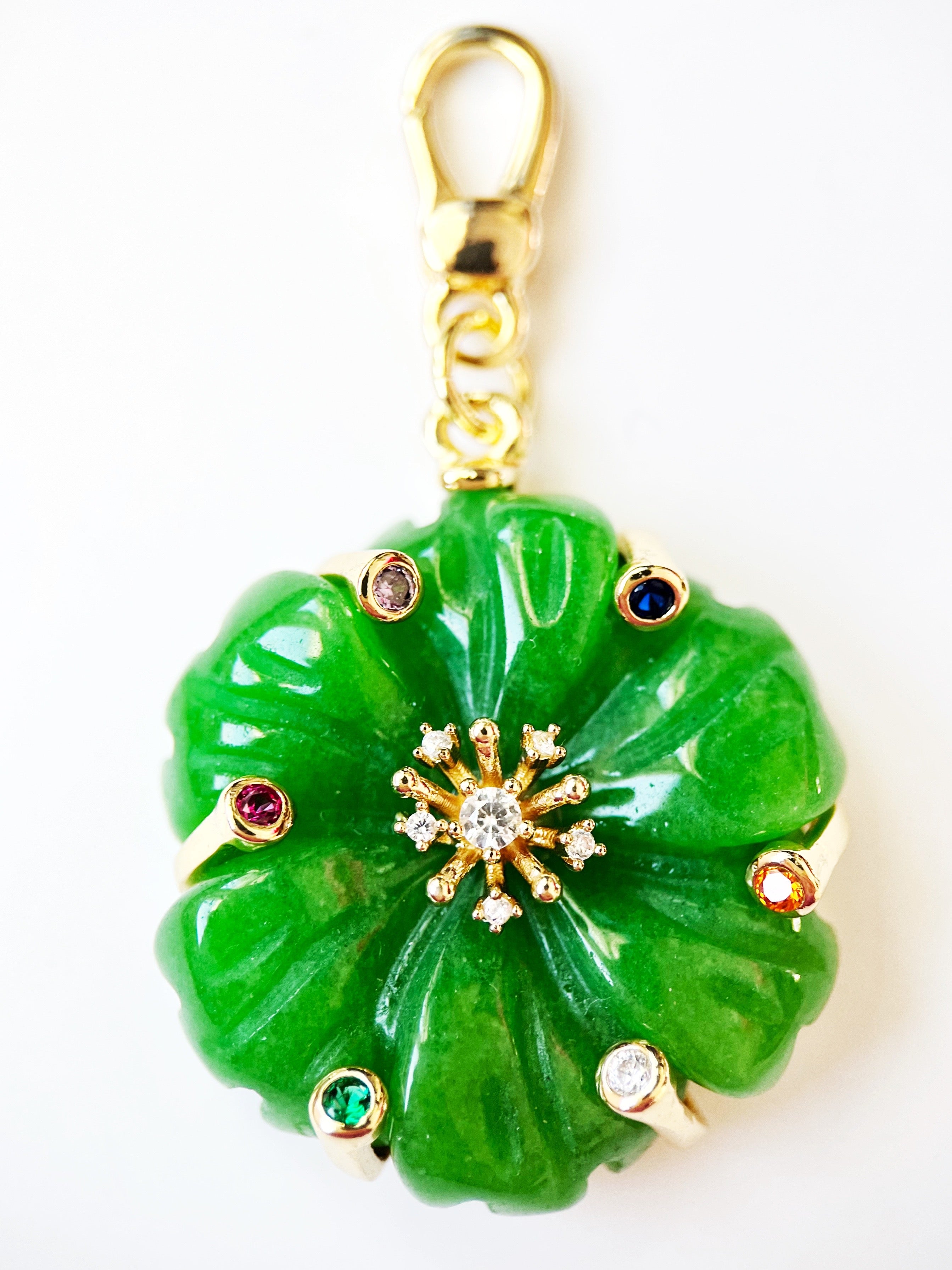 Green jade flower pendant with gold and gemstone accents on a white background