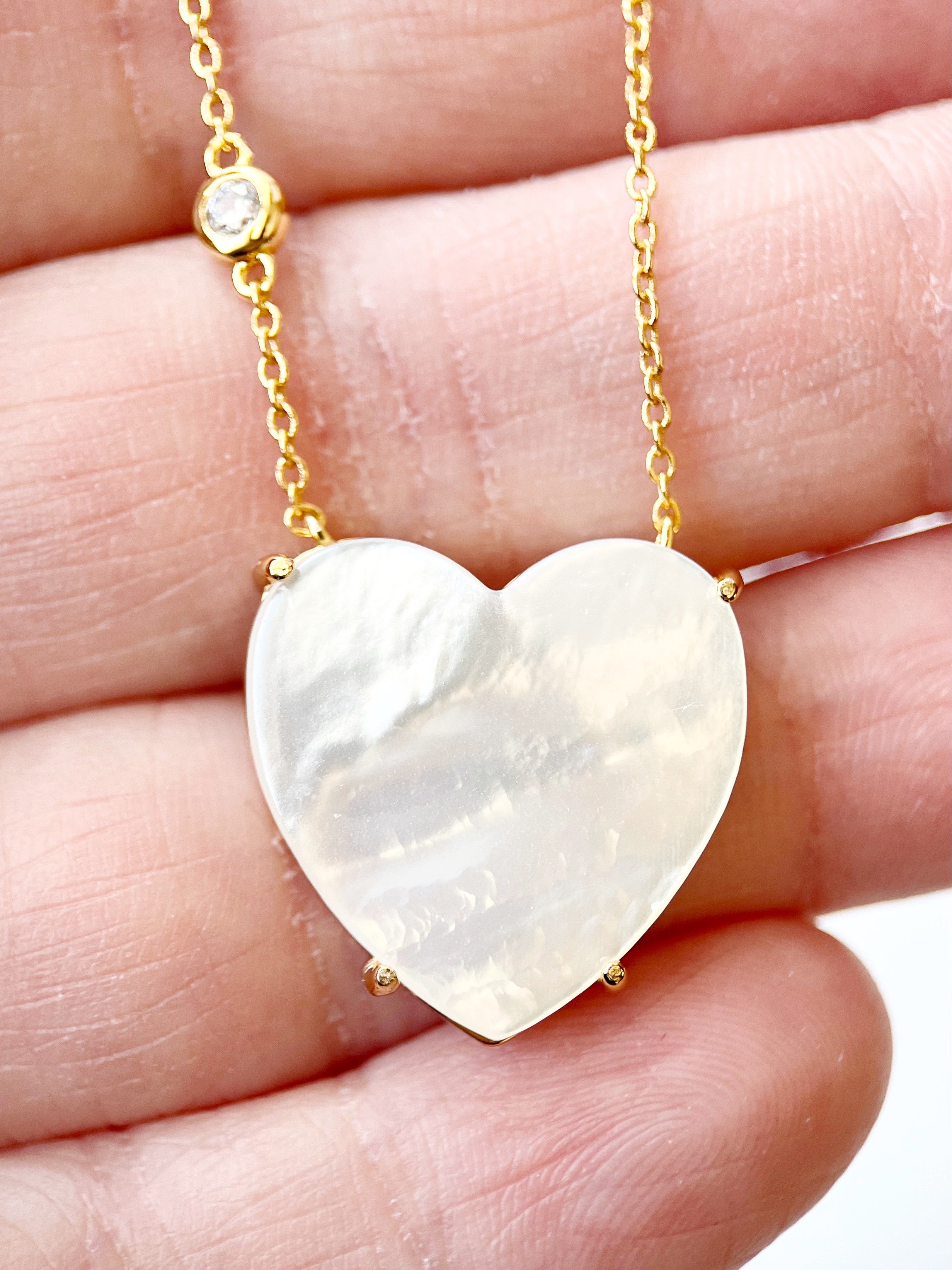 Heart-shaped pearl pendant on a gold chain held between fingers