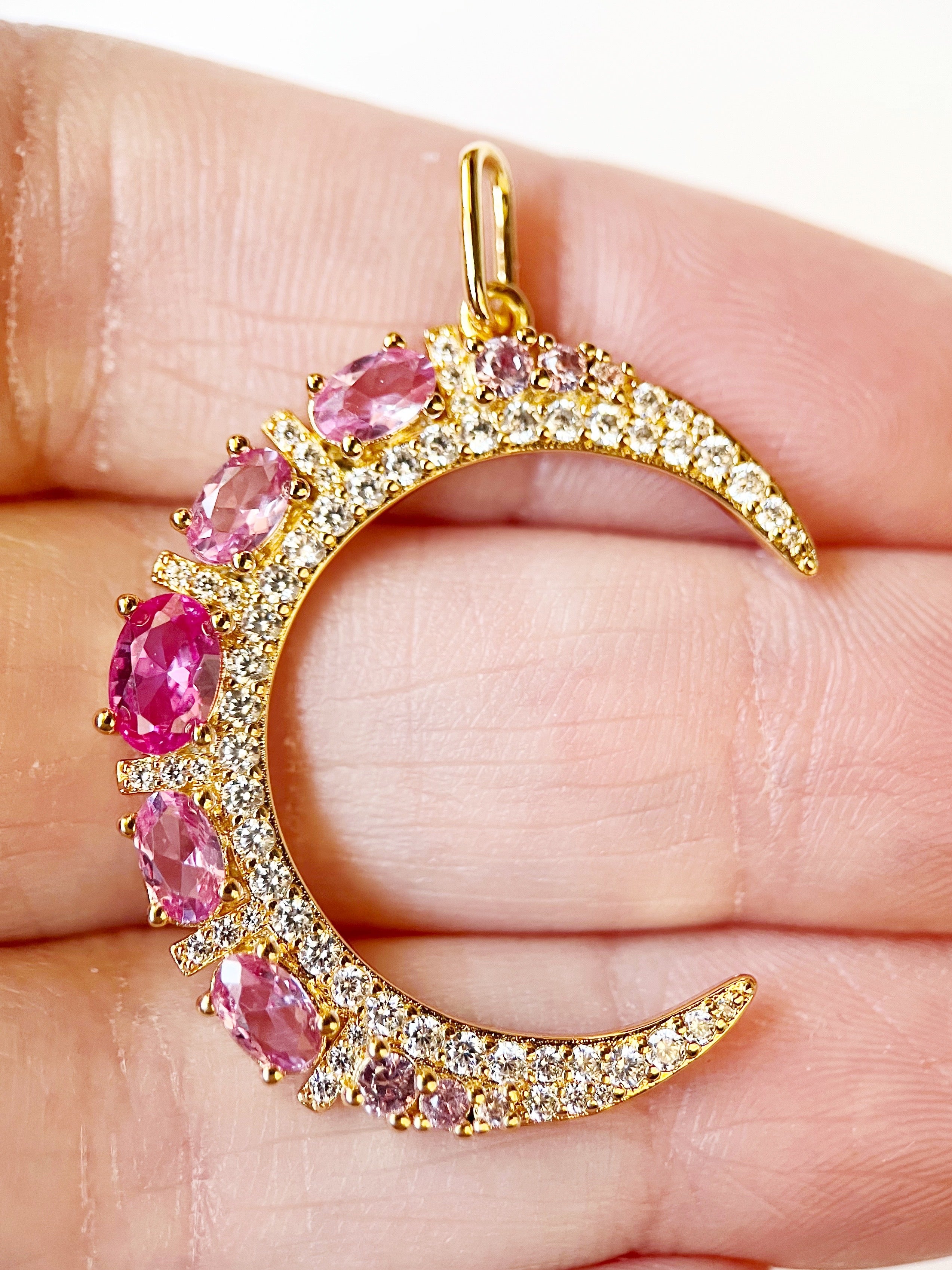 Gold crescent moon pendant with pink gemstones held between fingers