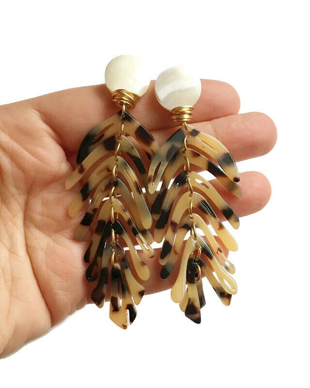 brown statement earrings held on a hand