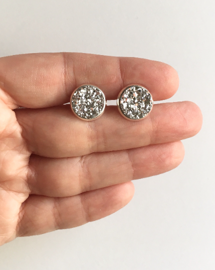 Hand holding Silver resin druzy stone stud setting is set in a yellow gold color setting between fingers.