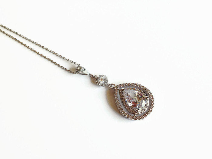 Teardrop cut cubic zirconia crystal with round halo accent set in silver color rhodium plated brass pendant necklace.