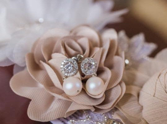 Cubic zirconia crystal stud earrings with white pear dangles sitting in flowers.