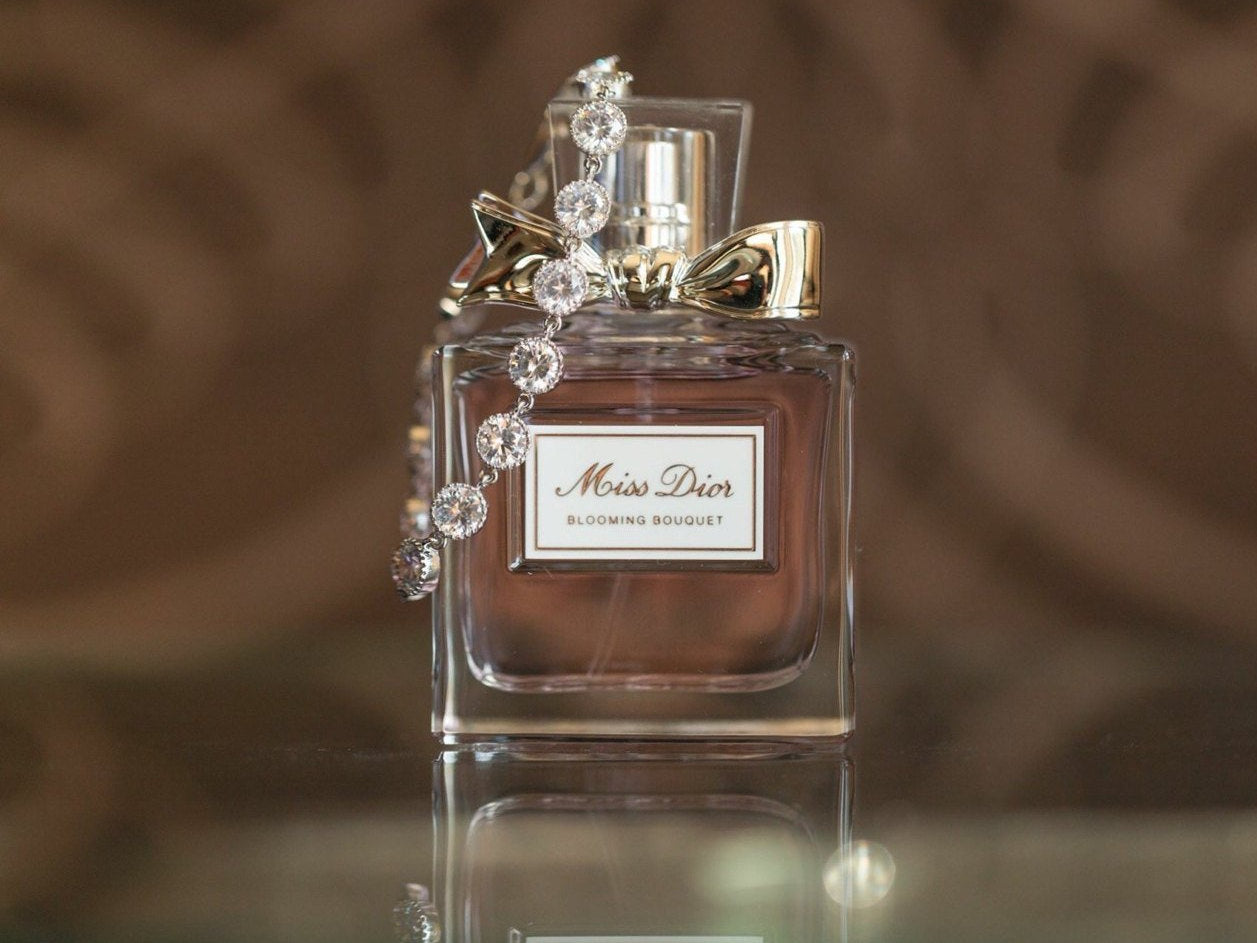 Cubic zirconia crystals set in silver color rhodium plated brass bracelet displayed on perfume bottle.