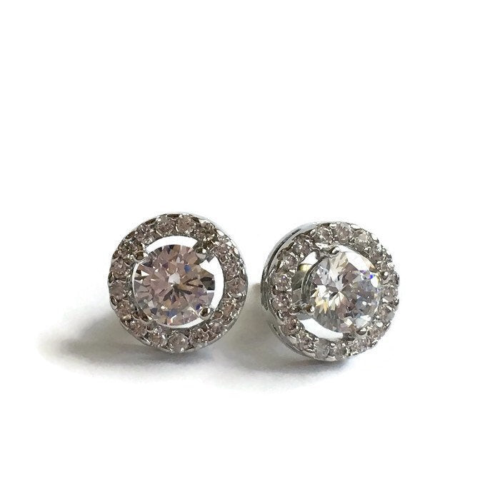 Round cubic zirconia halo stud earrings in a silver colored rhodium plated brass setting. 