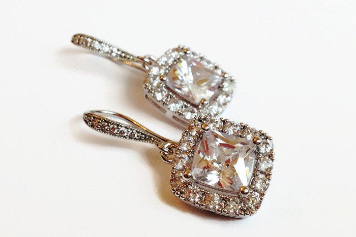 Cubic zirconia square crystal dangle earrings in a silver colored rhodium plated brass setting.