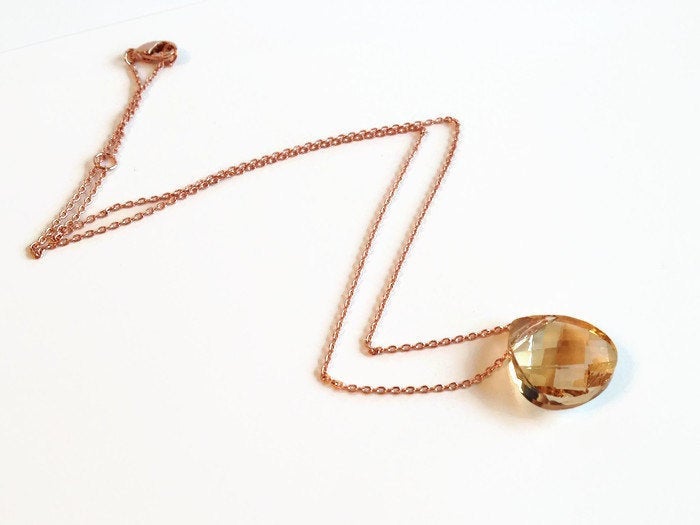golden shadow teardrop crystal Pendant Necklace with Adjustable Chain laying on table.