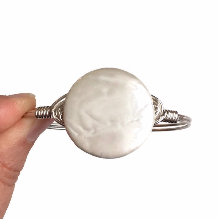 Coin Pearl and Silver Bangle statement Bracelet held up by fingers.