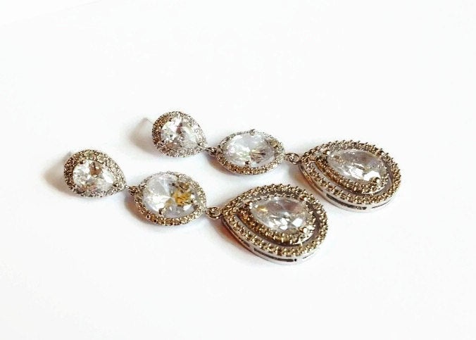 Cubic zirconia teardrop crystals in a silver colored rhodium plated brass setting statement chandelier earrings.