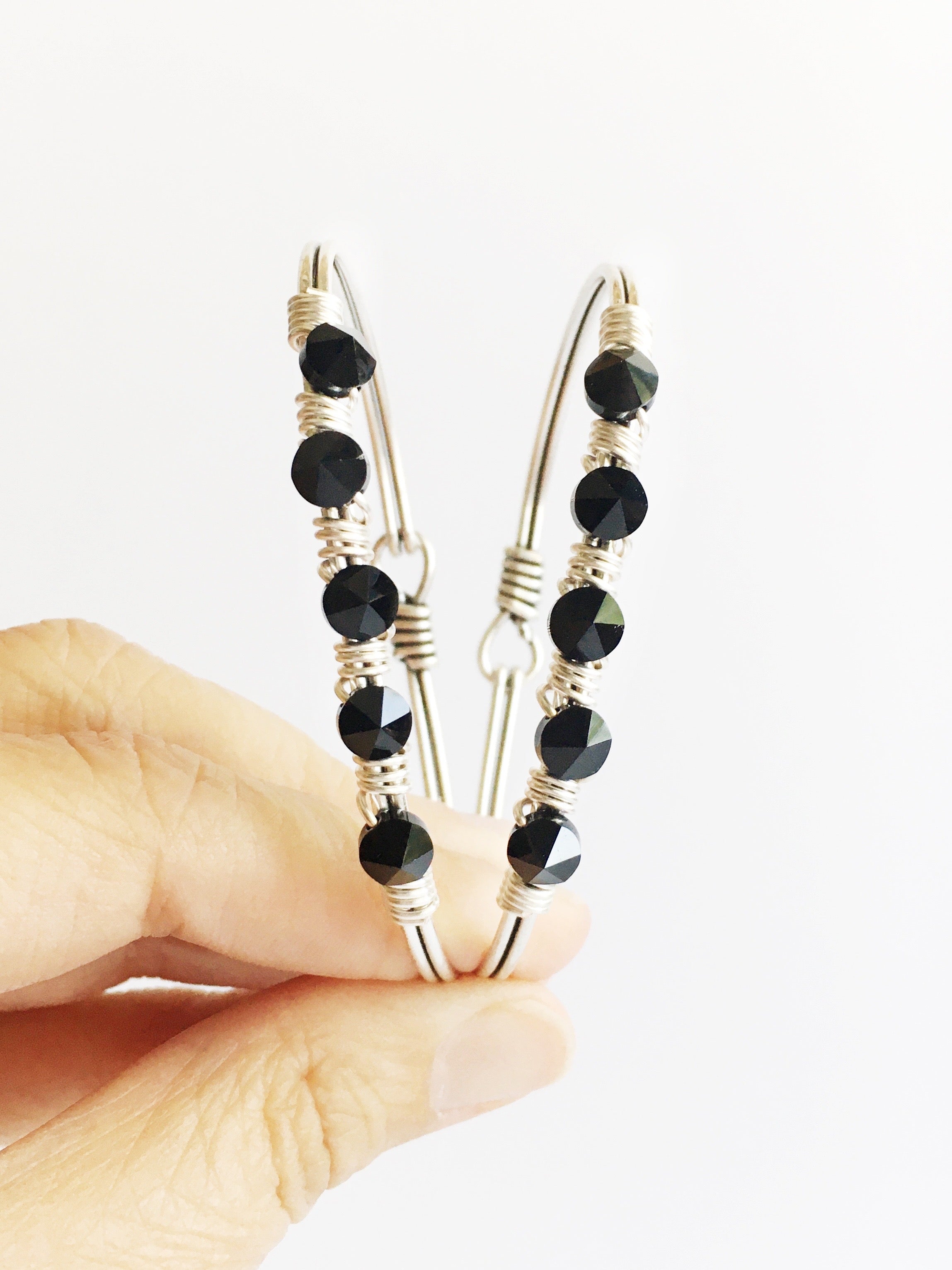 Two Hand wired black crystals and silver bangle bracelets being held up