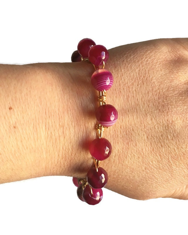 Women's wrist wearing pink agate gemstone and gold bangle bracelet.