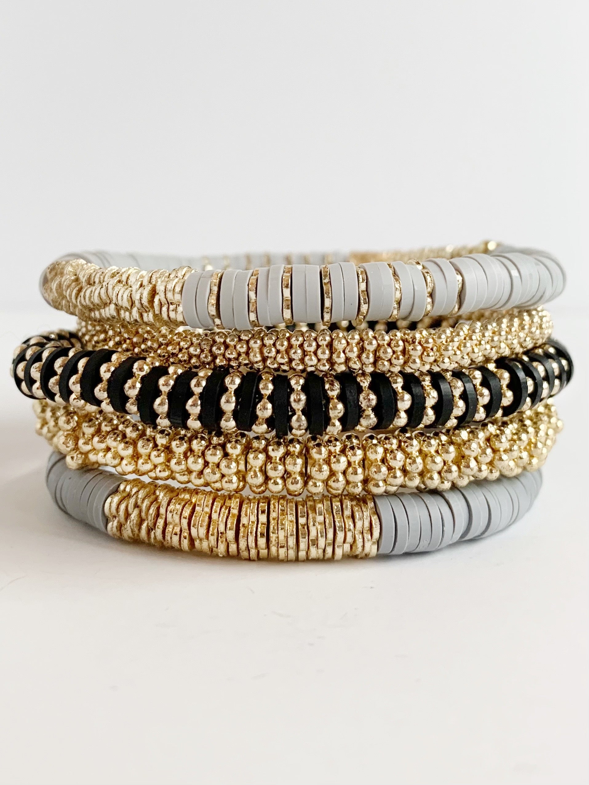 Bundle of stretch bracelets stacked together - they are -light gray confetti bracelet -small gold confetti bracelet -medium gold confetti bracelet -dark gray confetti bracelet -black and gold (the rosella) confetti bracelet