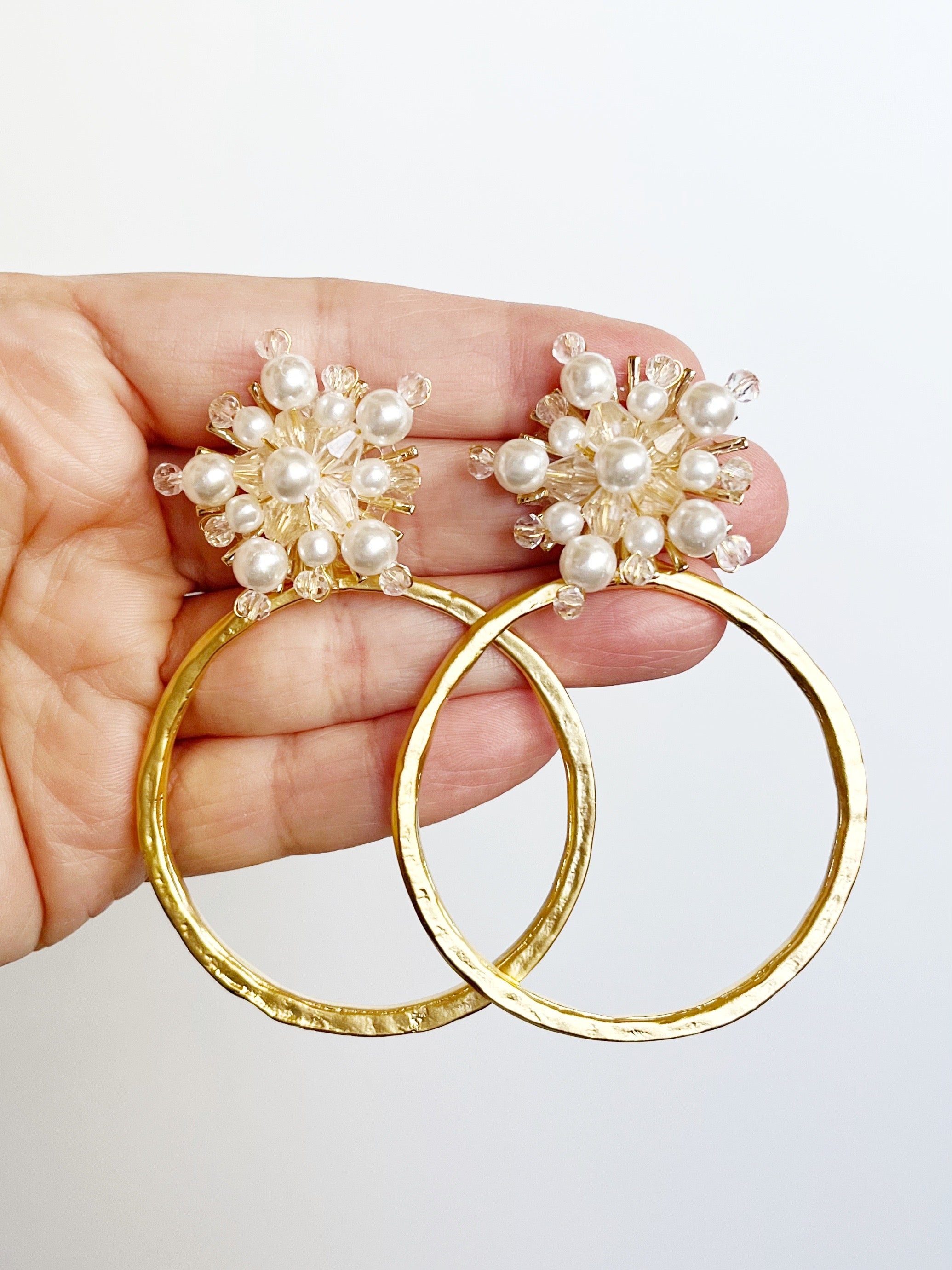 yellow gold hoop statement earrings with crystal and pearl stud displayed on handl