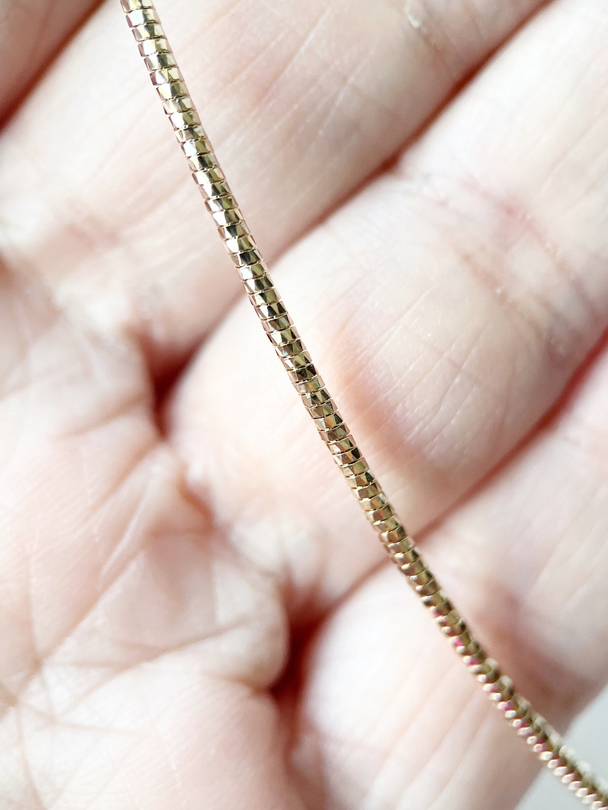 A close-up of a hand holding a thin, gold-toned chain necklace