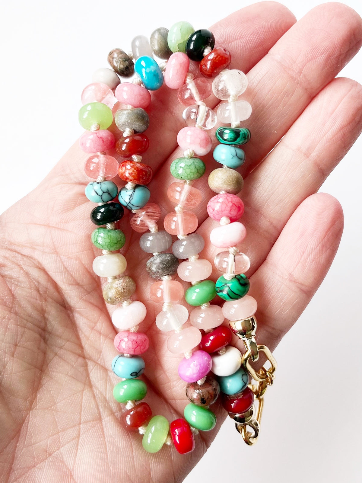 A close-up of a hand holding a beaded necklace made of colorful polished gemstone beads 