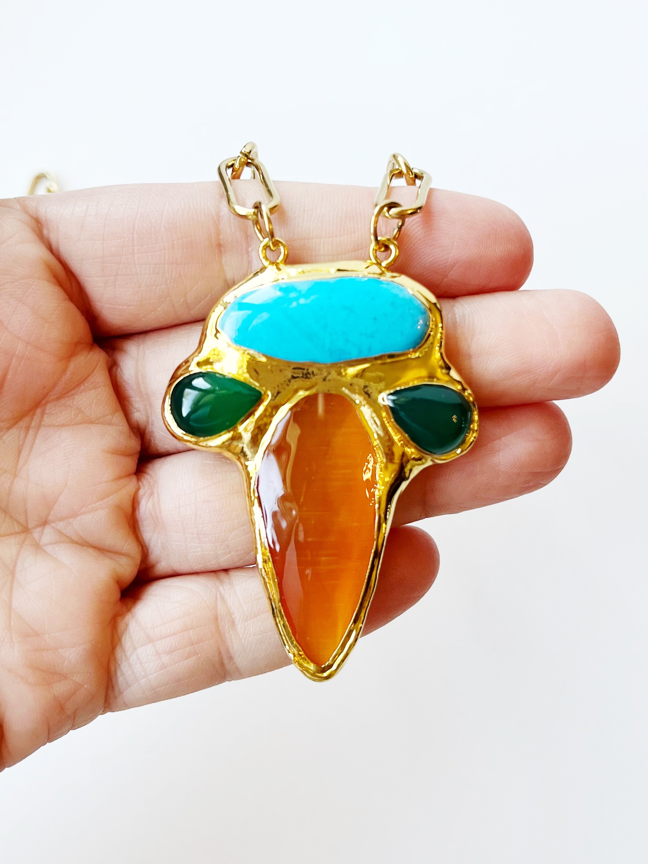 Hand holding a colorful pendant with gold frame on a white background