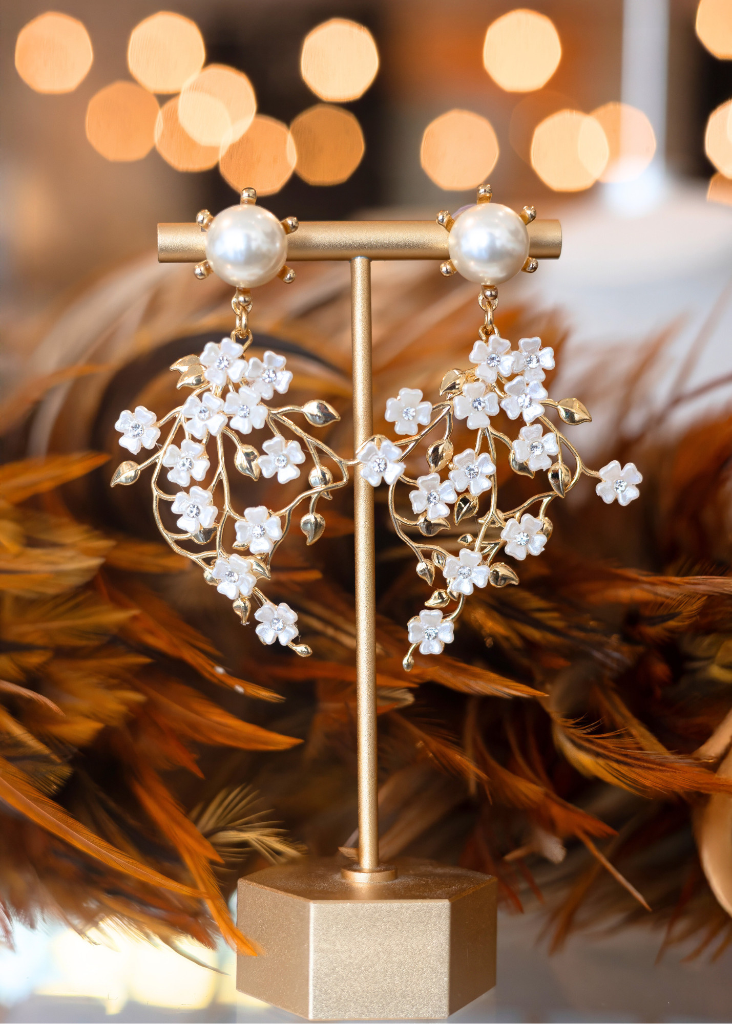 Gold earrings with floral design on a gold stand against a blurred background