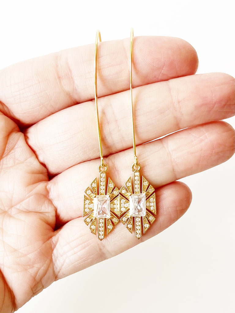 long gold earrings with crystal accents displayed on hand