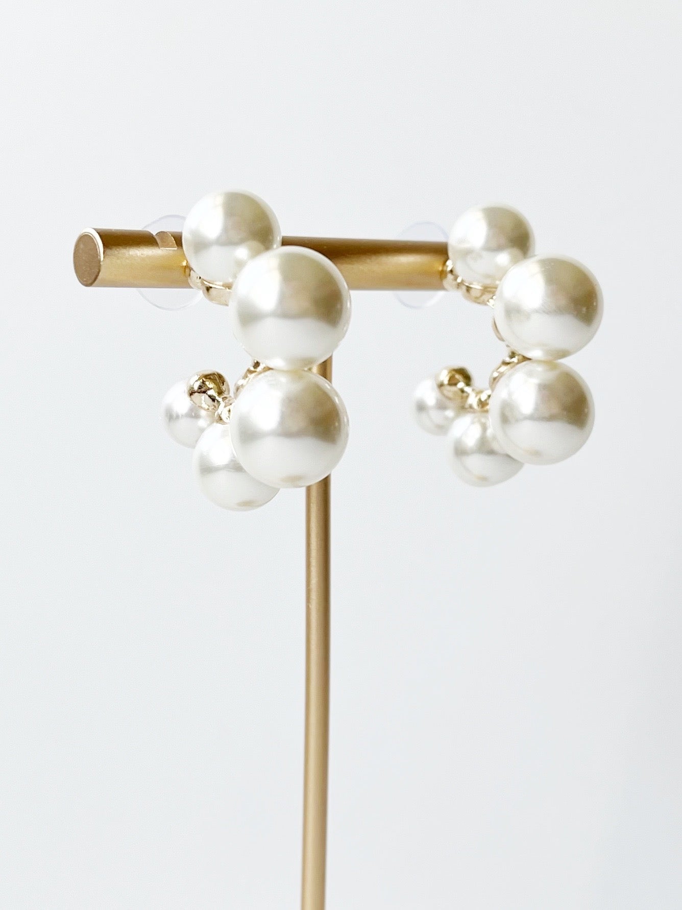 Pair of pearl earrings on a gold stand against a white background