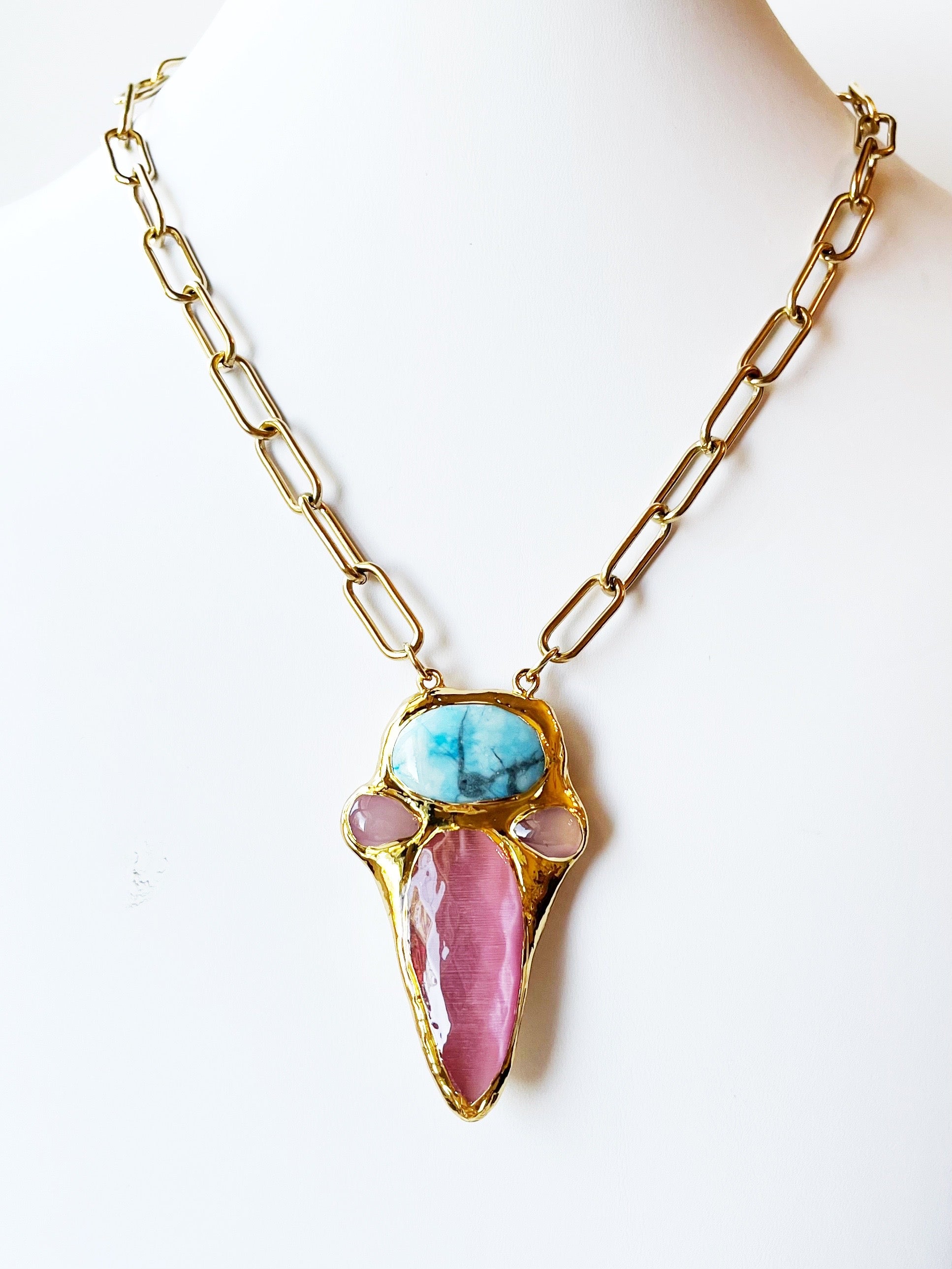 Necklace with pink and blue stone pendant on gold chain against a white background