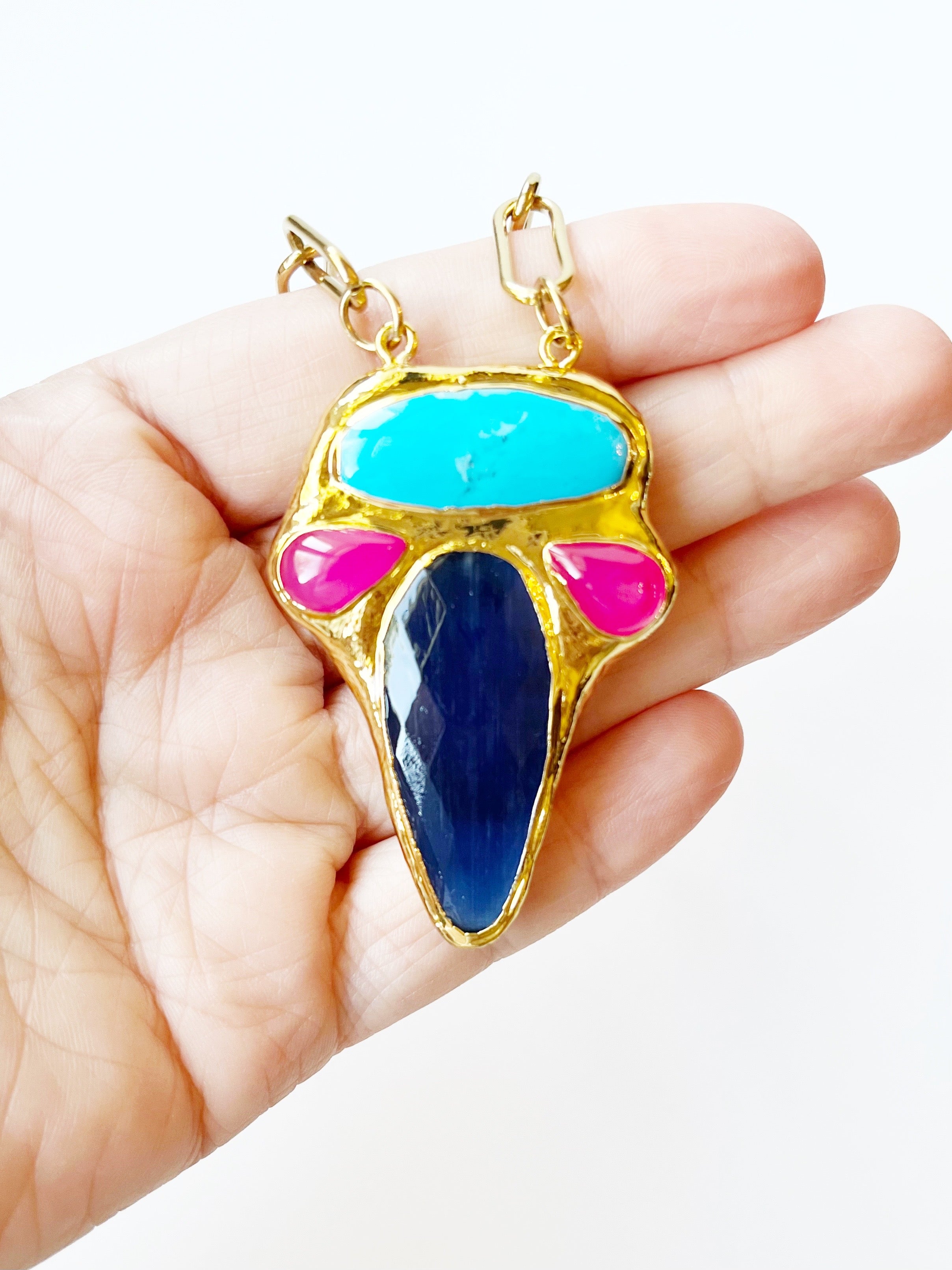 Colorful pendant with gold frame held in a hand against a white background