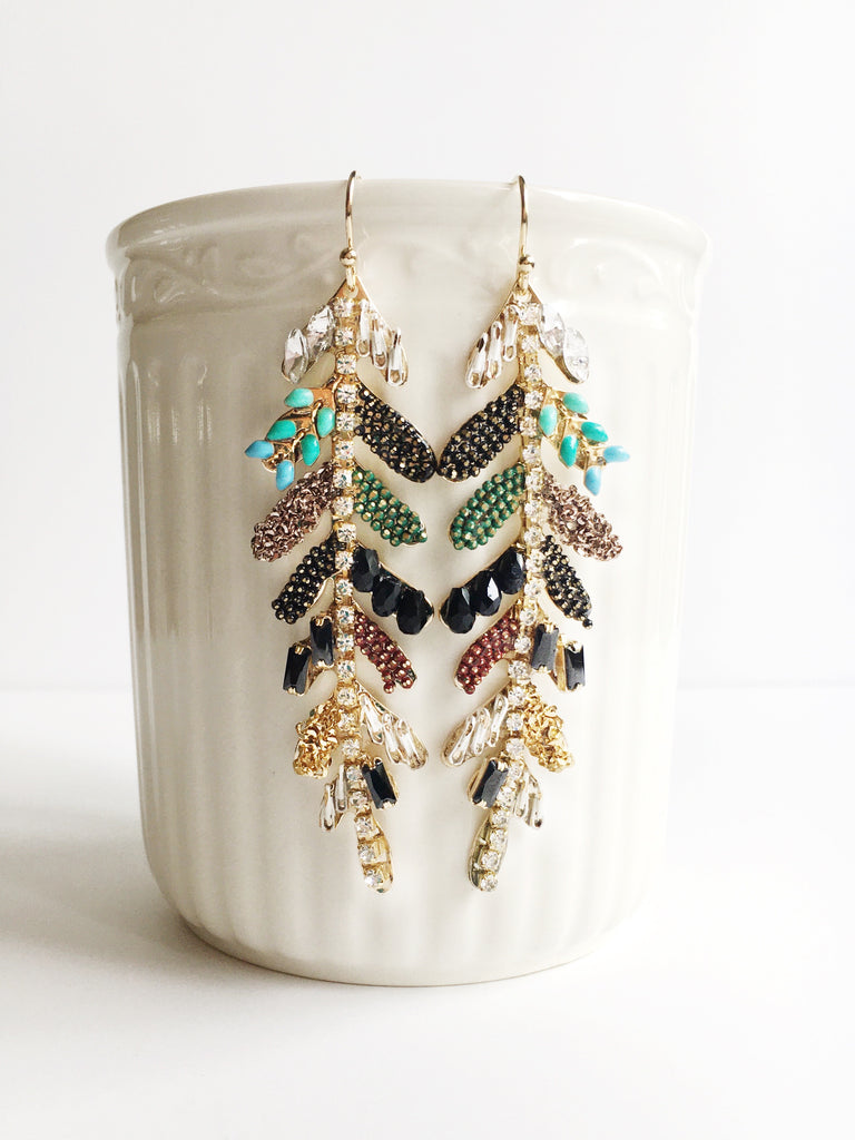 Gold leaf adorned with crystals and elements drop earrings hanging from white coffee mug