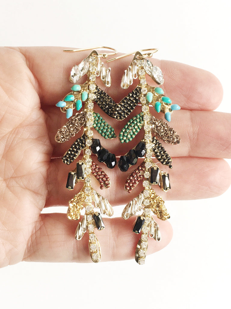 Gold leaf adorned with crystals and elements drop earrings hand in women's hand.