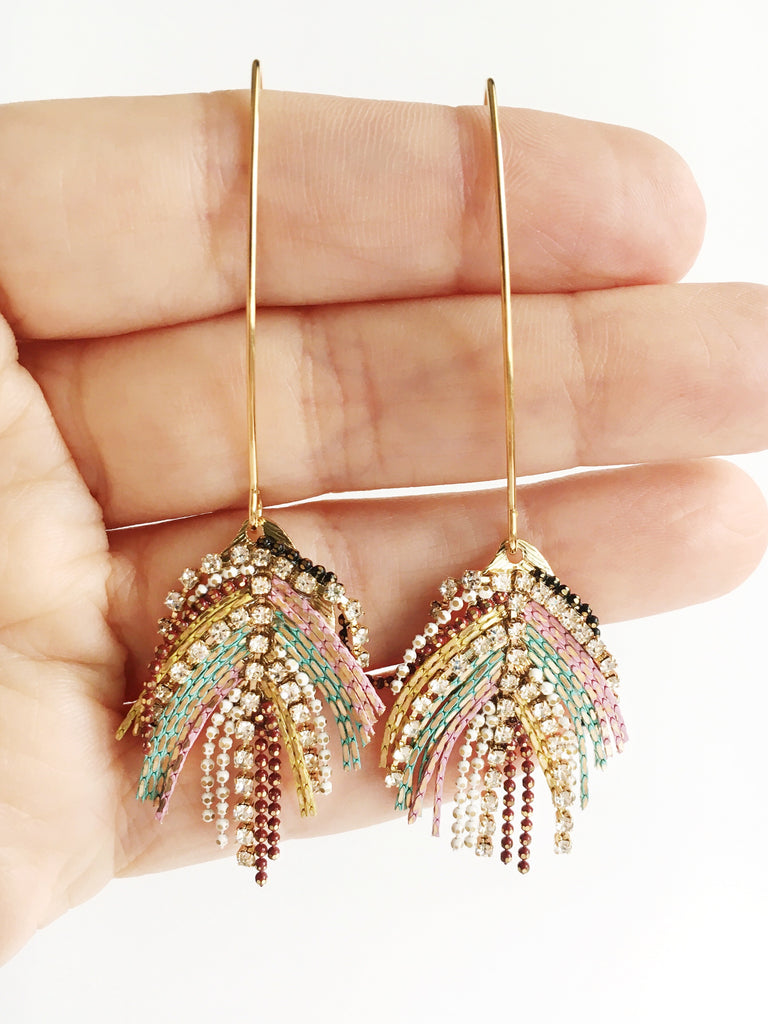 Hand holding Gold drop dangle peacock colored earrings