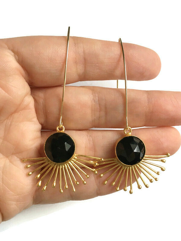 Gold sunburst and black onyx statement earrings held in hand