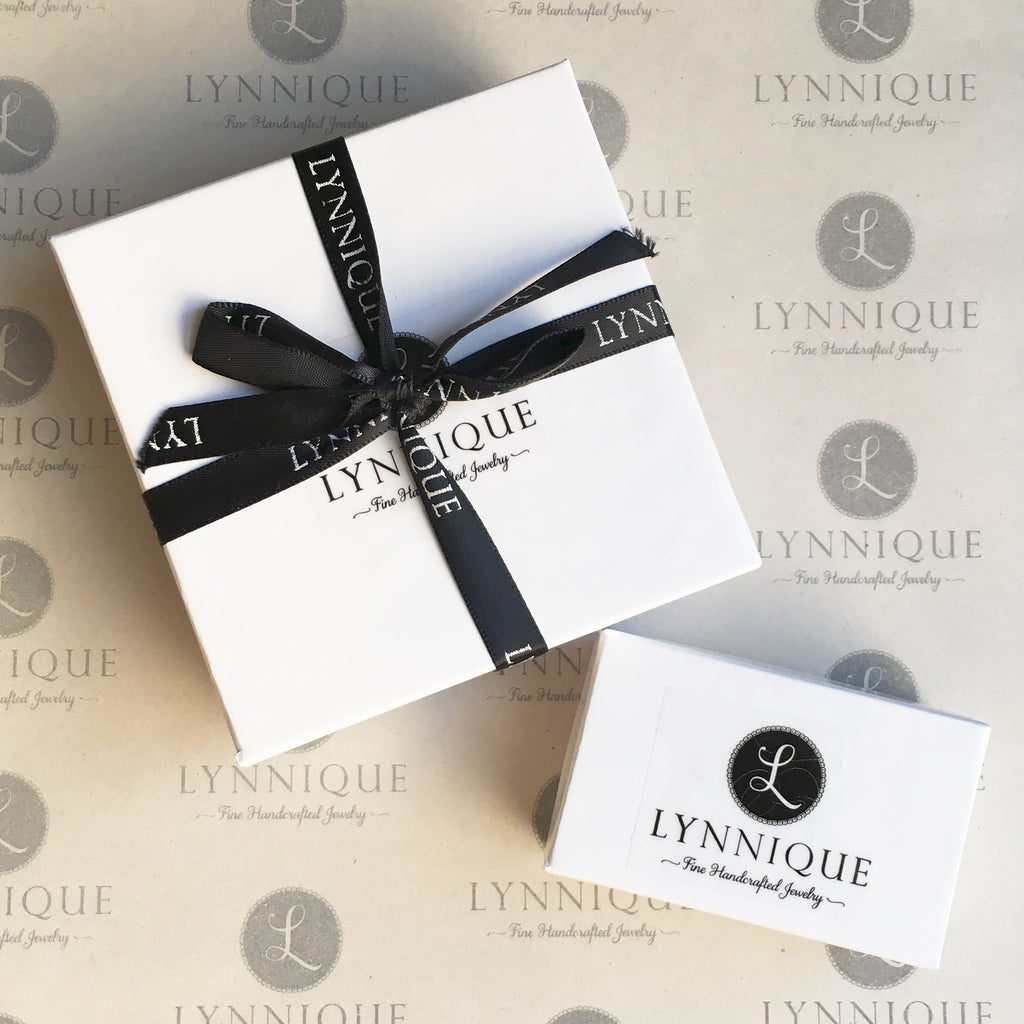 white jewelry boxes with branded label and black ribbon tied in a bow with text that reads LYNNIQUE
