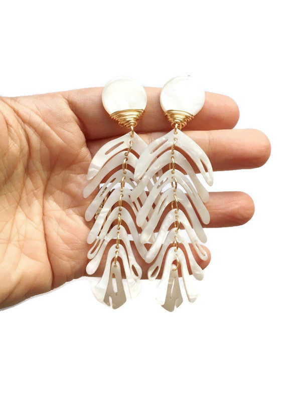 white statement earrings held on hand