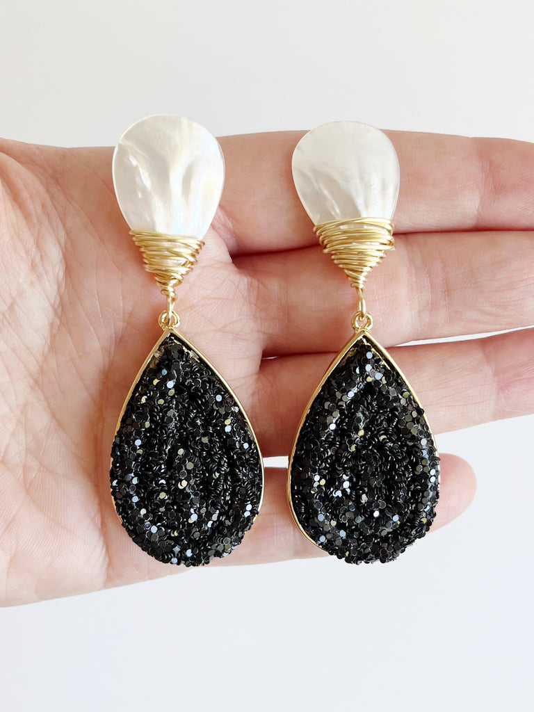 black glitter teardrop earrings with mother of pearl stud displayed on hand