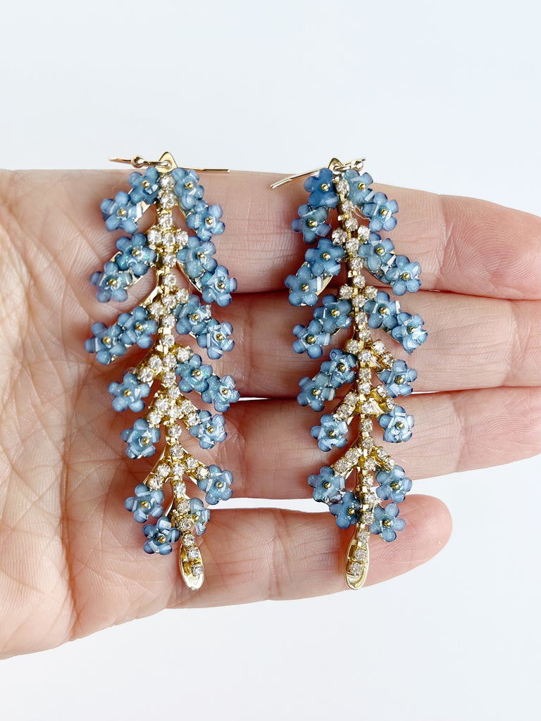 gold leaf statement earrings with cubic zirconia and blue glass flowers displayed on hand