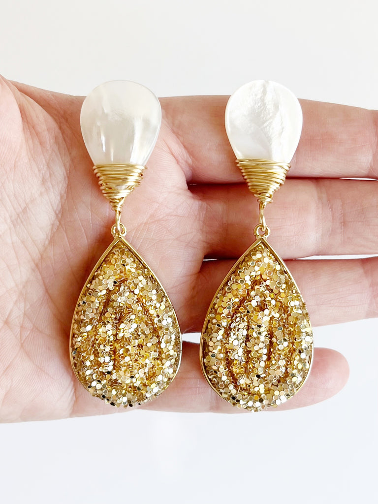 gold glitter teardrop earrings with mother of pearl stud displayed on hand