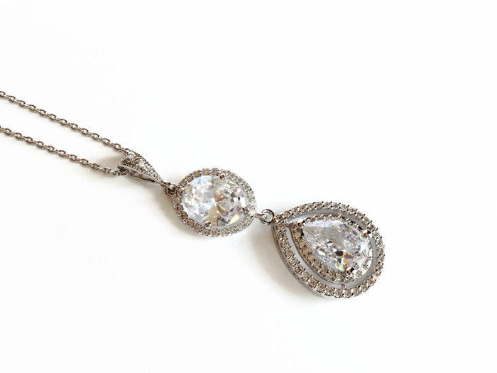 Teardrop cut cubic zirconia crystal with round oval accent set in silver color rhodium plated brass pendant necklace.