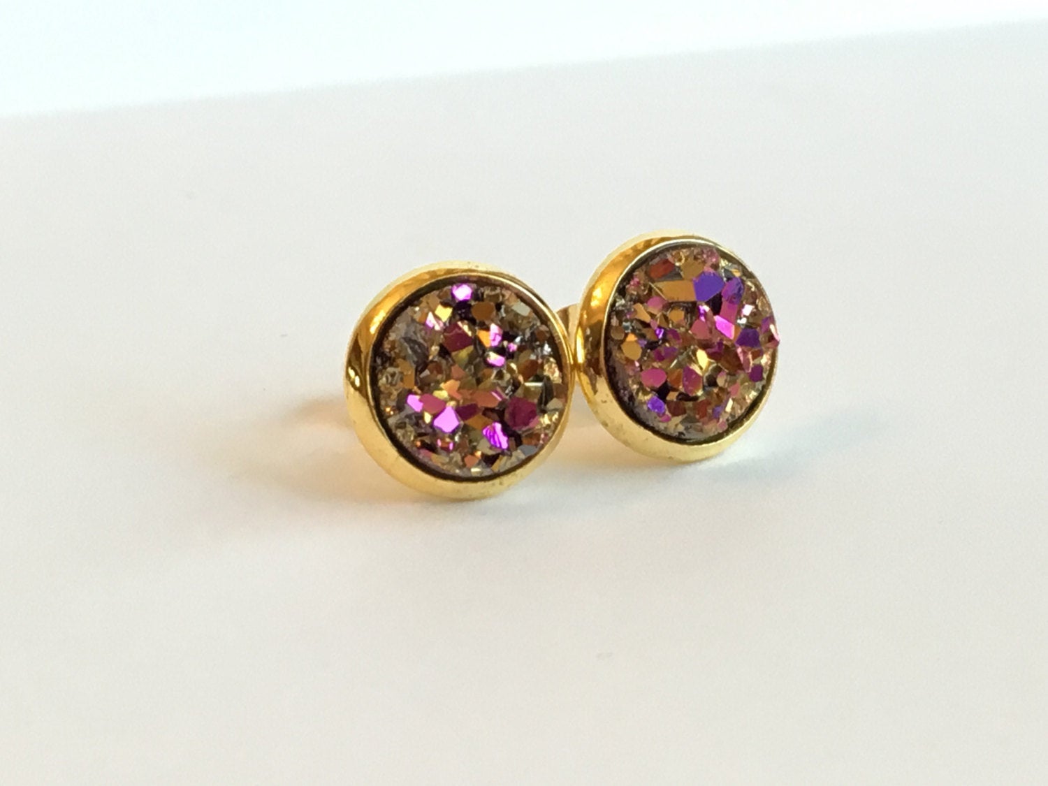 Angled view of Pink and gold resin druzy stone stud earrings set in a yellow gold color setting