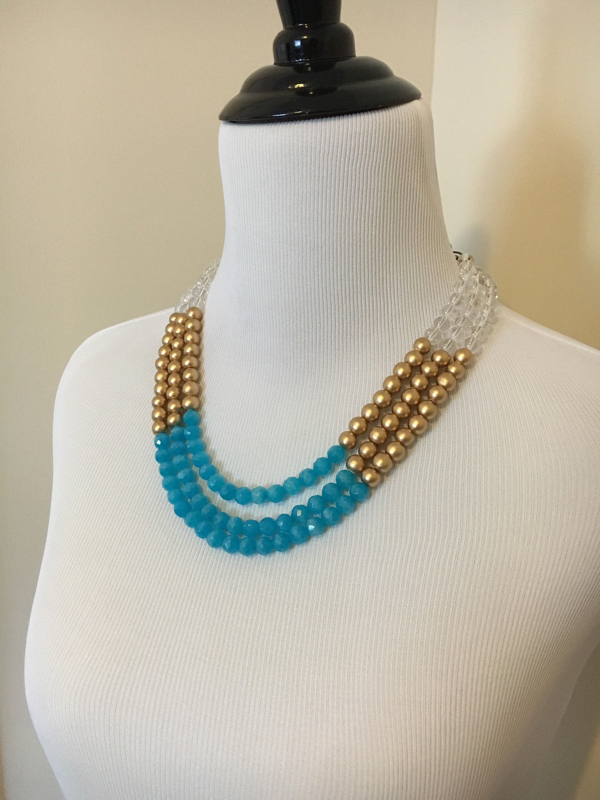 Side view of mannequin wearing Three strand teal jade, clear quartz, and gold wooden bead statement necklace