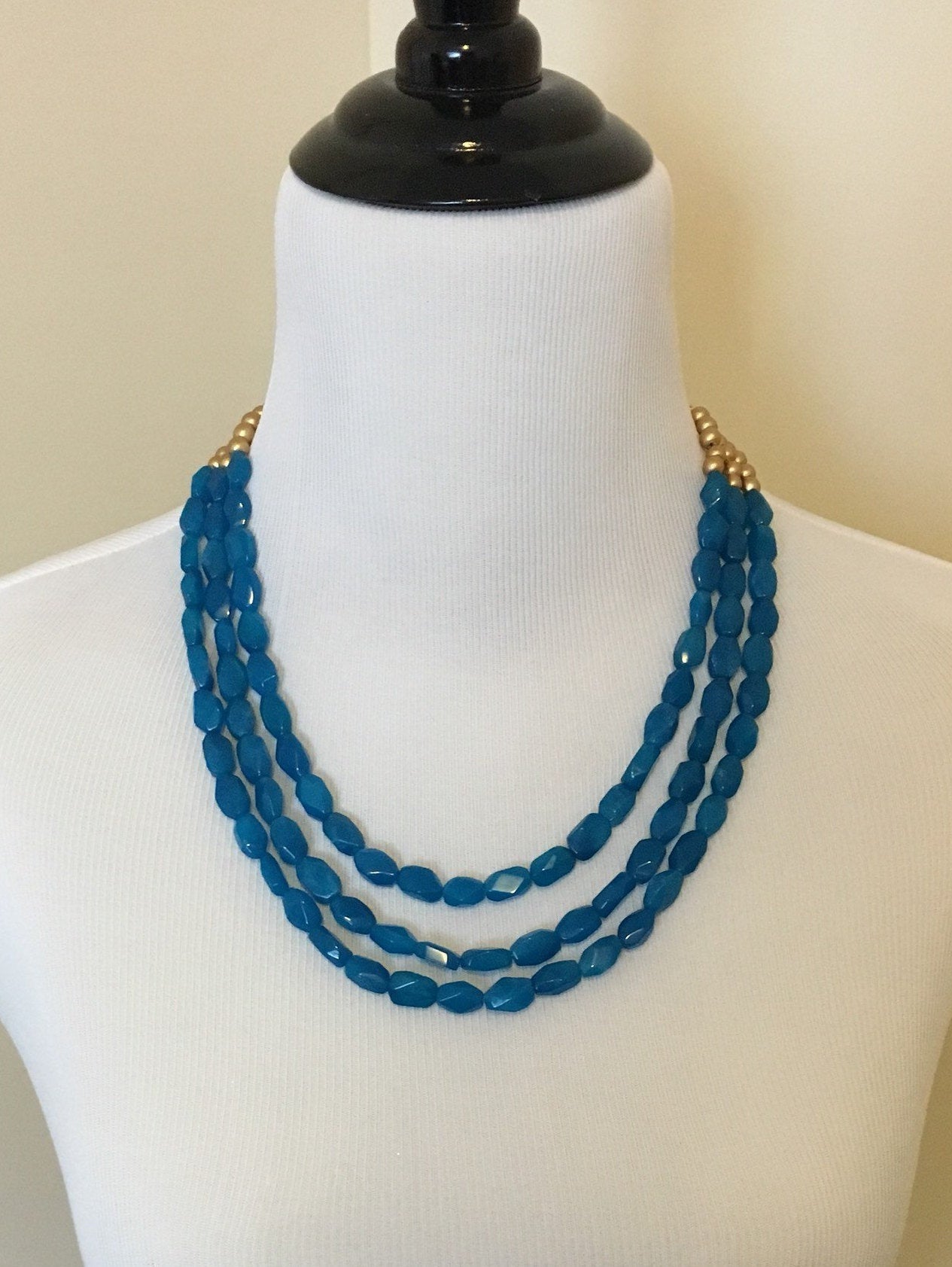 Mannequin wearing Three strand turquoise quartz and gold wooden beaded necklace close up.