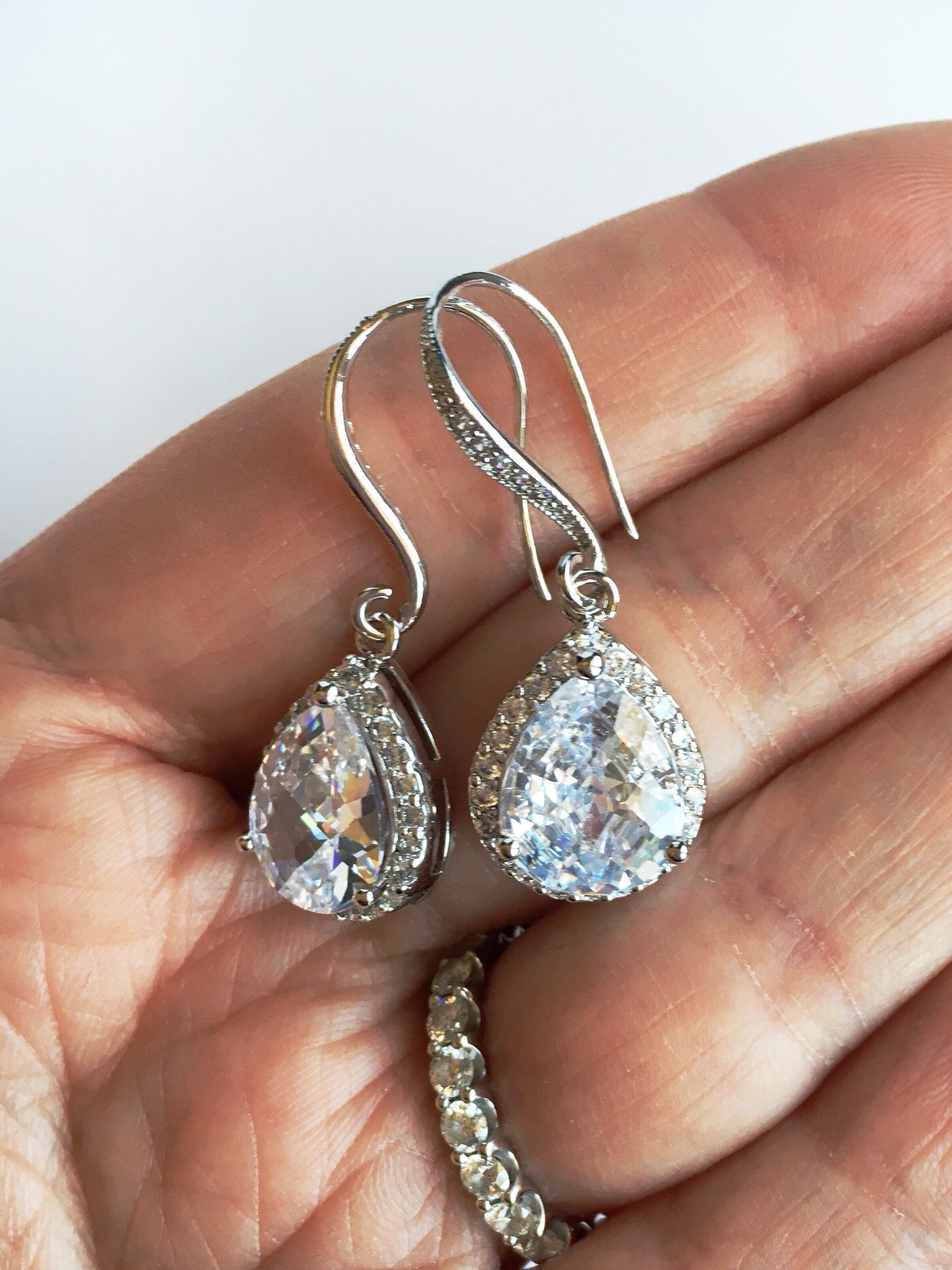 Women holding Clear cubic zirconia teardrop crystals in a silver colored rhodium plated brass setting earrings in hand.