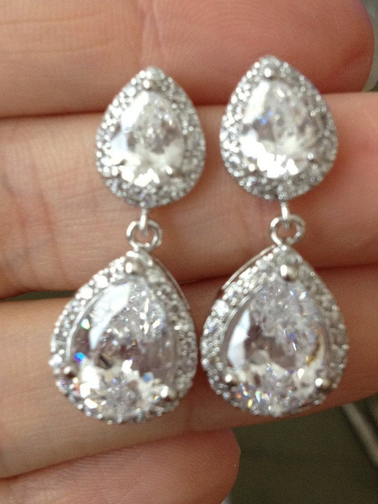 Hand holding Clear cubic zirconia teardrop crystals in a silver colored rhodium plated brass setting earrings.