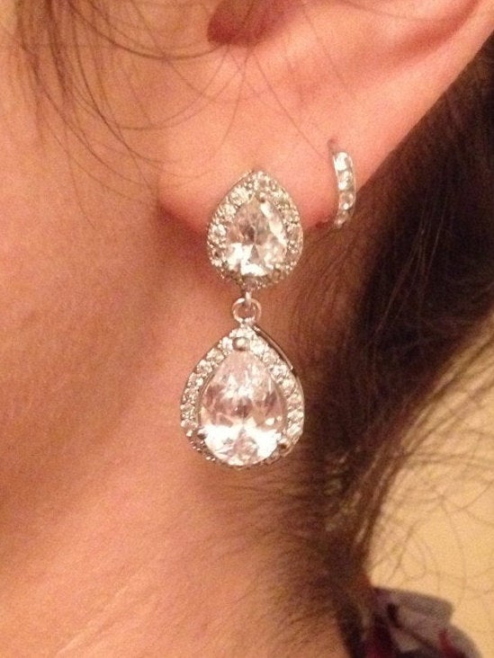 Women's ear wearing Clear cubic zirconia teardrop crystals in a silver colored rhodium plated brass setting earrings.