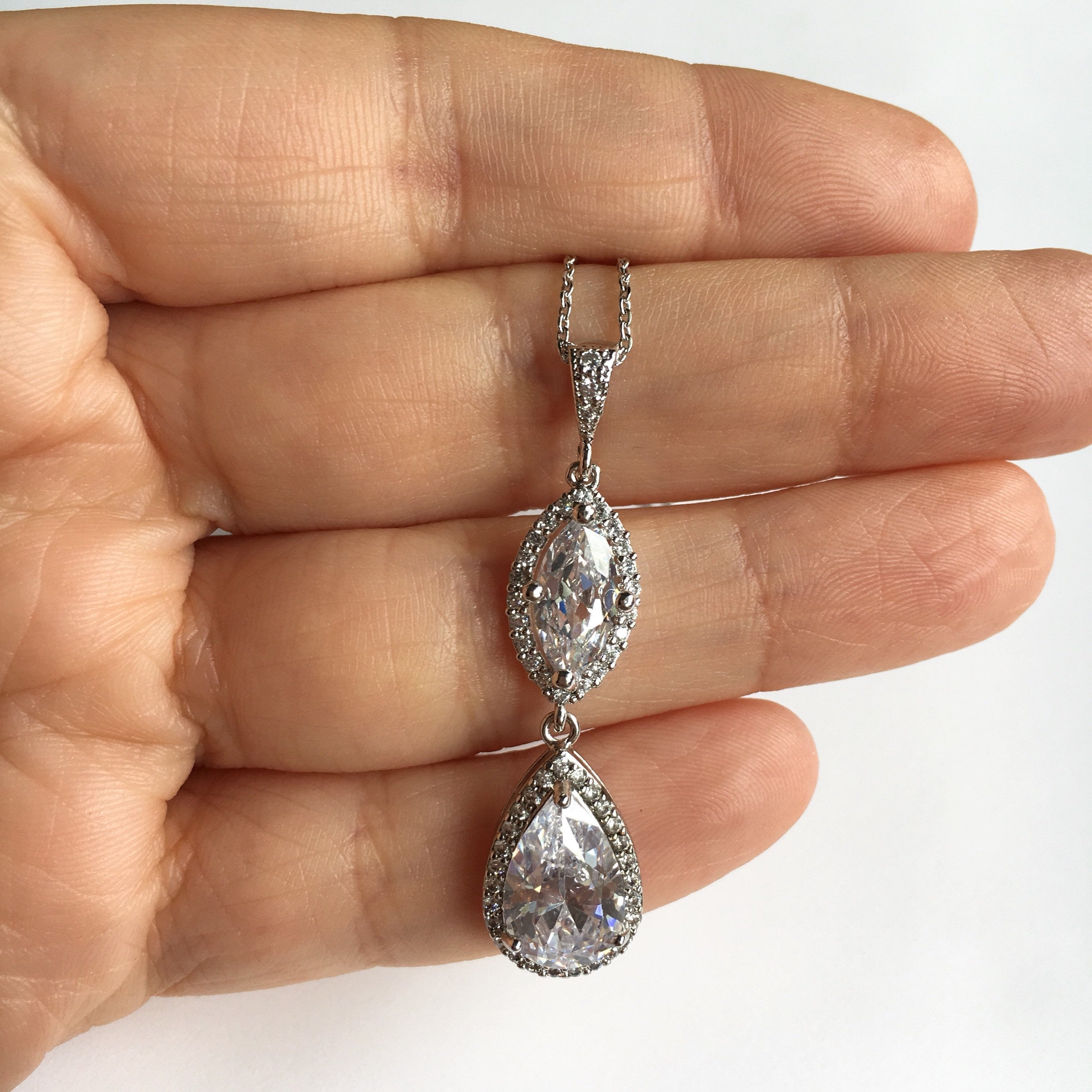 Cubic zirconia crystals set in silver color rhodium plated brass pendant necklace held in hand.
