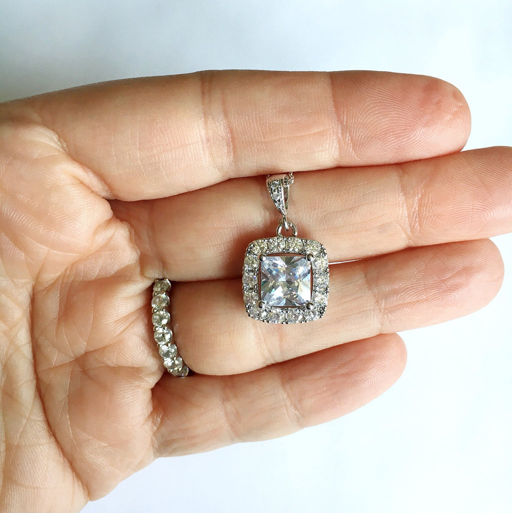 Hand holding Square cut cubic zirconia pendant set in silver color rhodium plated brass necklace.