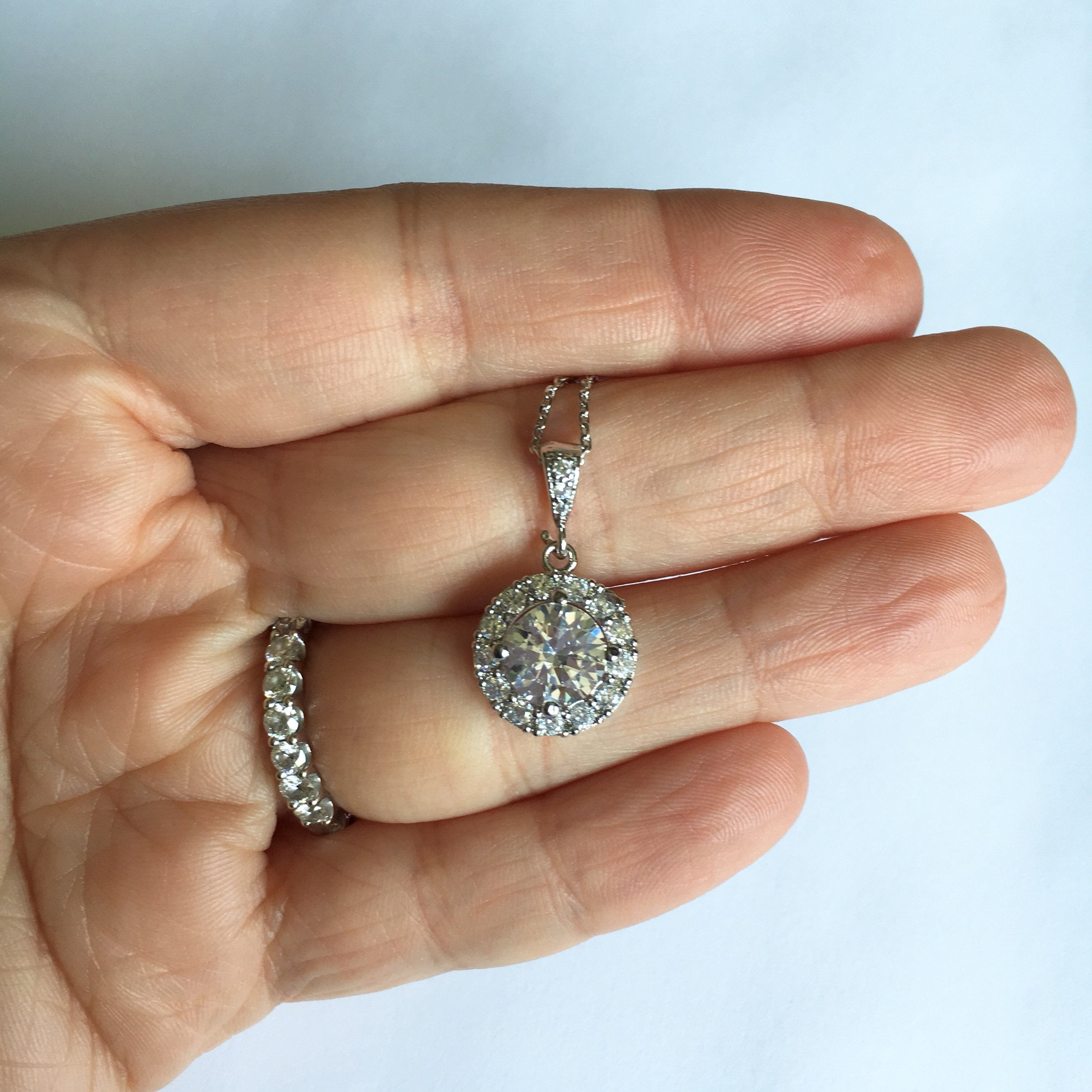 Hand holding Round cubic zirconia crystal necklace set in silver color rhodium plated brass pendant.