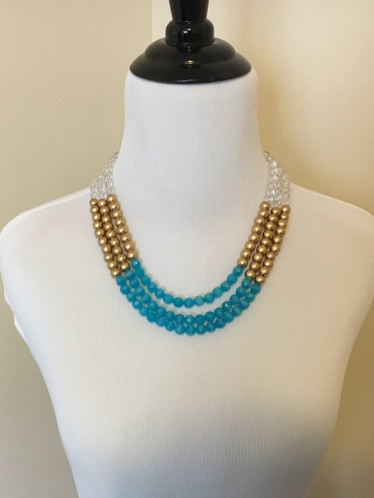 Front view of mannequin wearing Three strand teal jade, clear quartz, and gold wooden bead statement necklace
