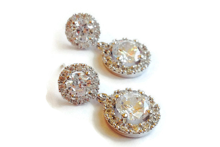 Round cubic zirconia Crystal Halo Dangle Earrings in a silver colored rhodium plated brass setting.