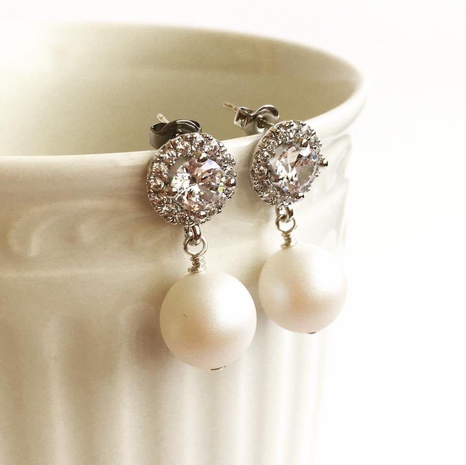 Cubic zirconia crystal stud earrings with white pear dangles hanging on coffee cup.