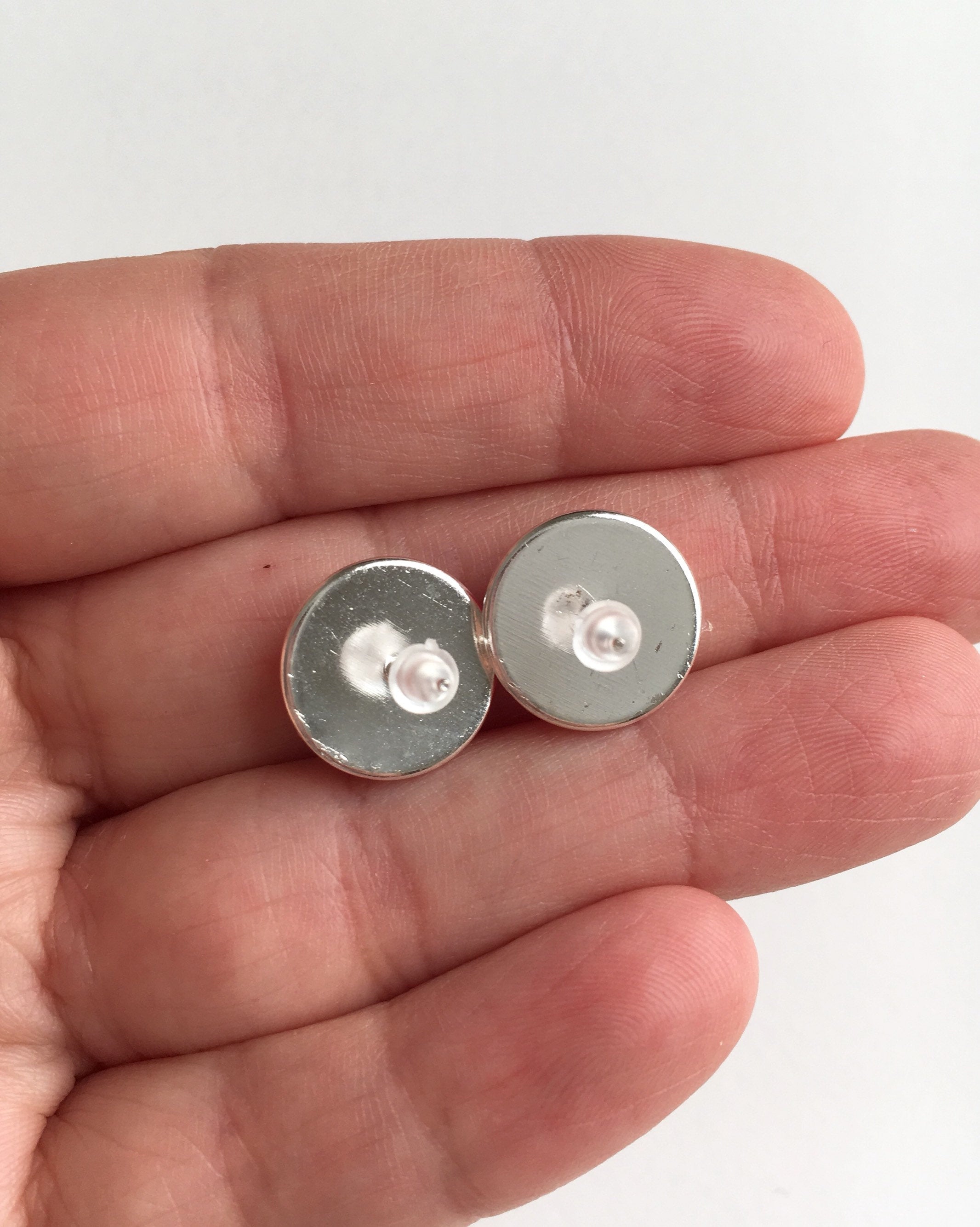 Back of silver setting stud earrings with rubber push back held in hand.